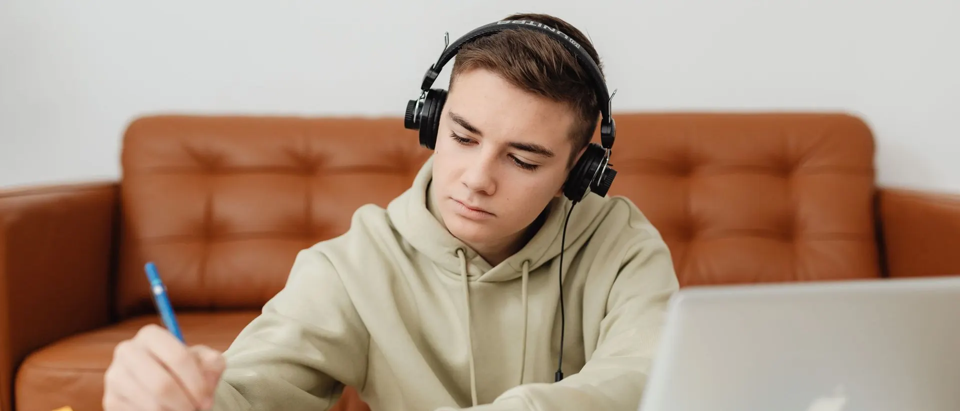 A teenager doing homework on a laptop with headphones on